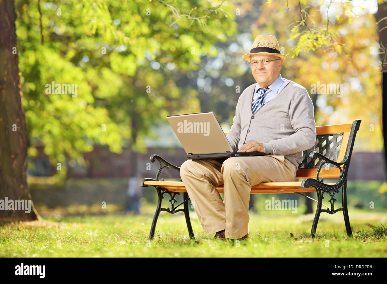 Senior gentleman lavorando su laptop seduto sulla panca di legno in posizione di parcheggio Foto Stock