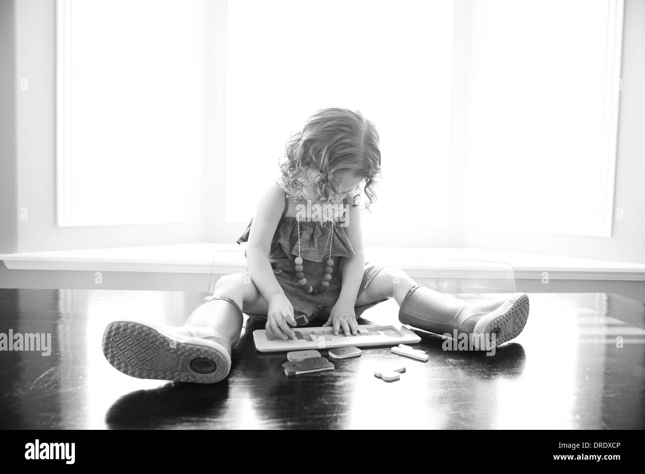 Poco ragazza seduta sulla scrivania mettendo insieme un puzzle Foto Stock