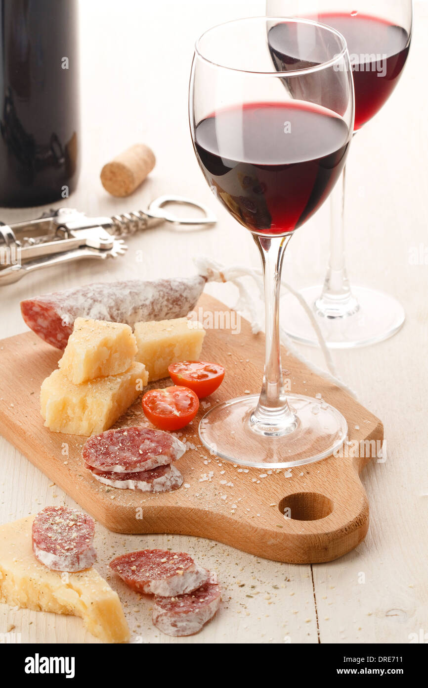 Due wineglasses con vino rosso e assortimento di formaggi e frutta su sfondo bianco Foto Stock