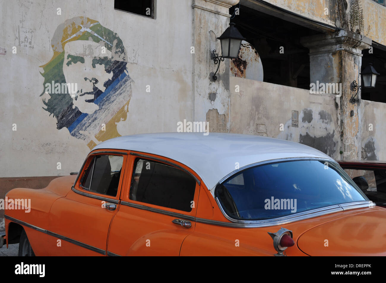 L'Avana, Cuba: Classic car parcheggiato a fianco di un murale di Che Guevara nel quartiere del porto della città . Foto Stock