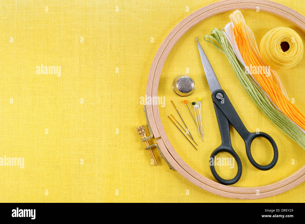 Ricamo e punto croce accessori giallo su tessuto di lino. Cerchio da ricamo, forbici, filo, aghi, ditale. Copia dello spazio. Foto Stock