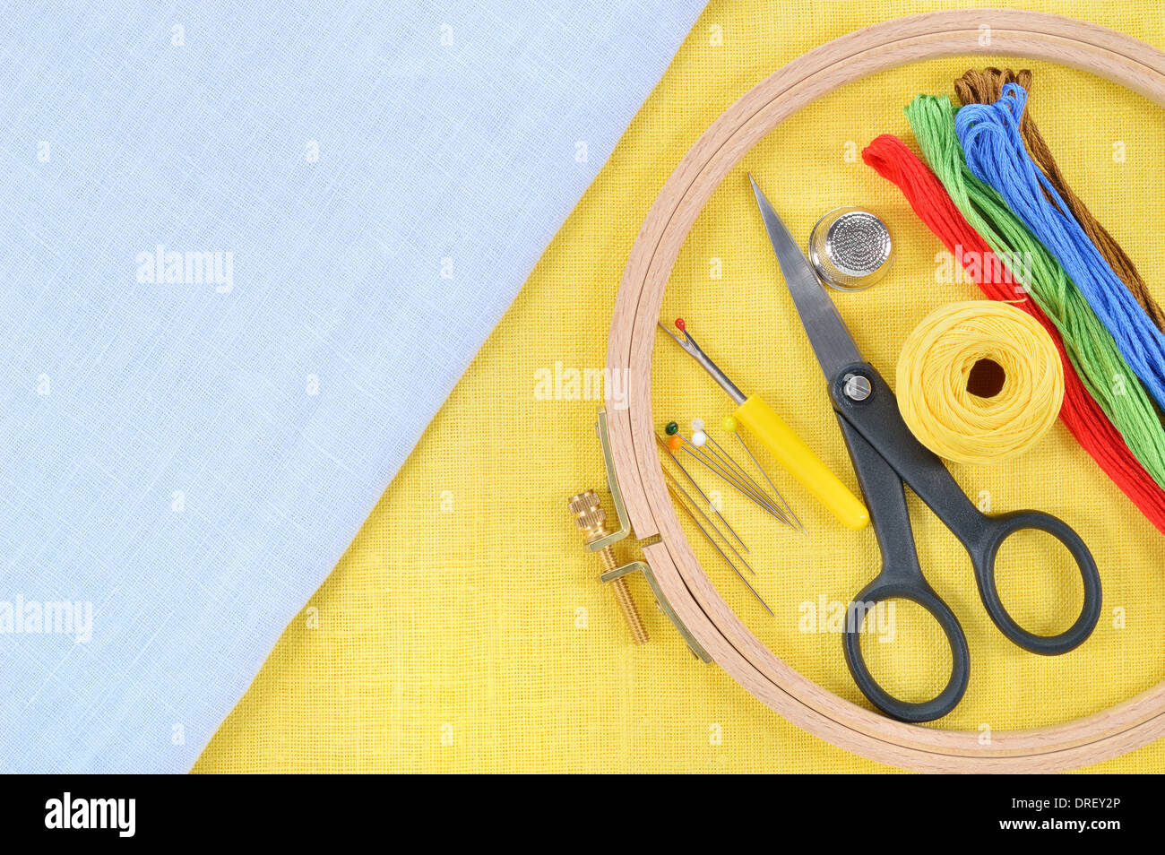 Ricamo e punto croce accessori sul giallo e azzurro tessuto di lino. Cerchio da ricamo, forbici, filo, aghi, thimb Foto Stock