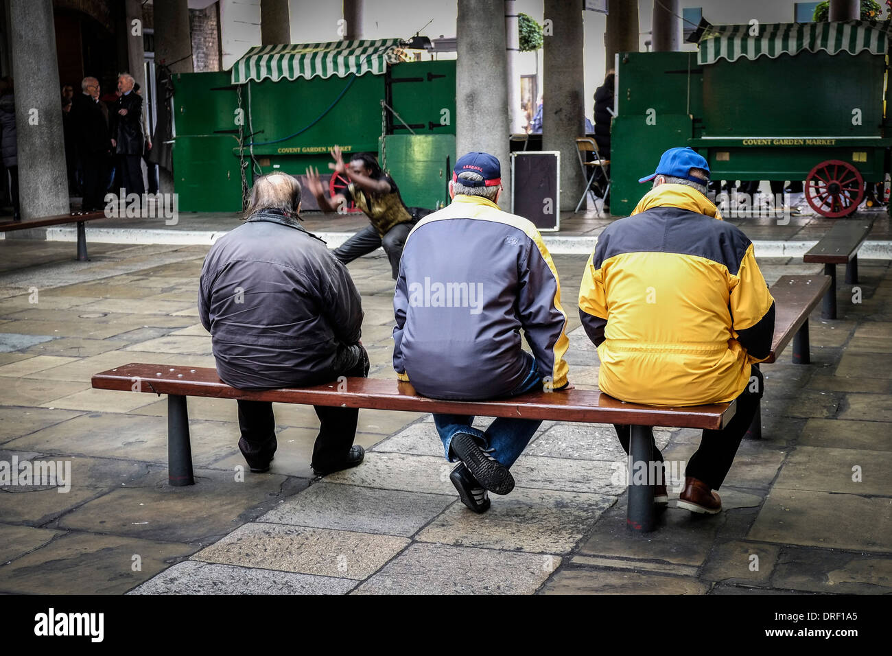 Tre uomini guardando un animatore di strada nel nord Hall di Covent Garden. Foto Stock