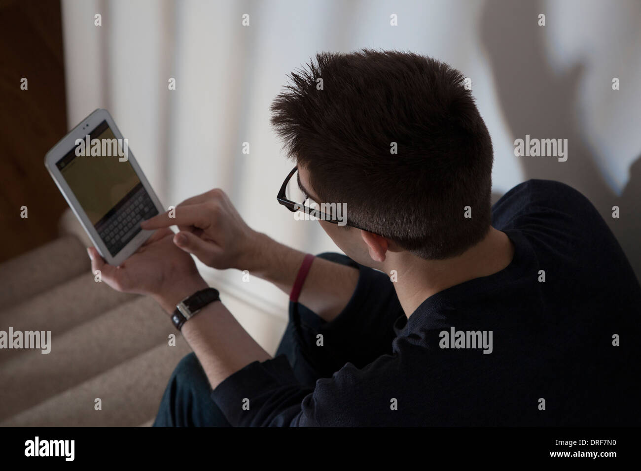 Sulla spalla colpo di uomo che indossa gli occhiali digitando su una tastiera sullo schermo a sfioramento digitale compressa. Foto Stock