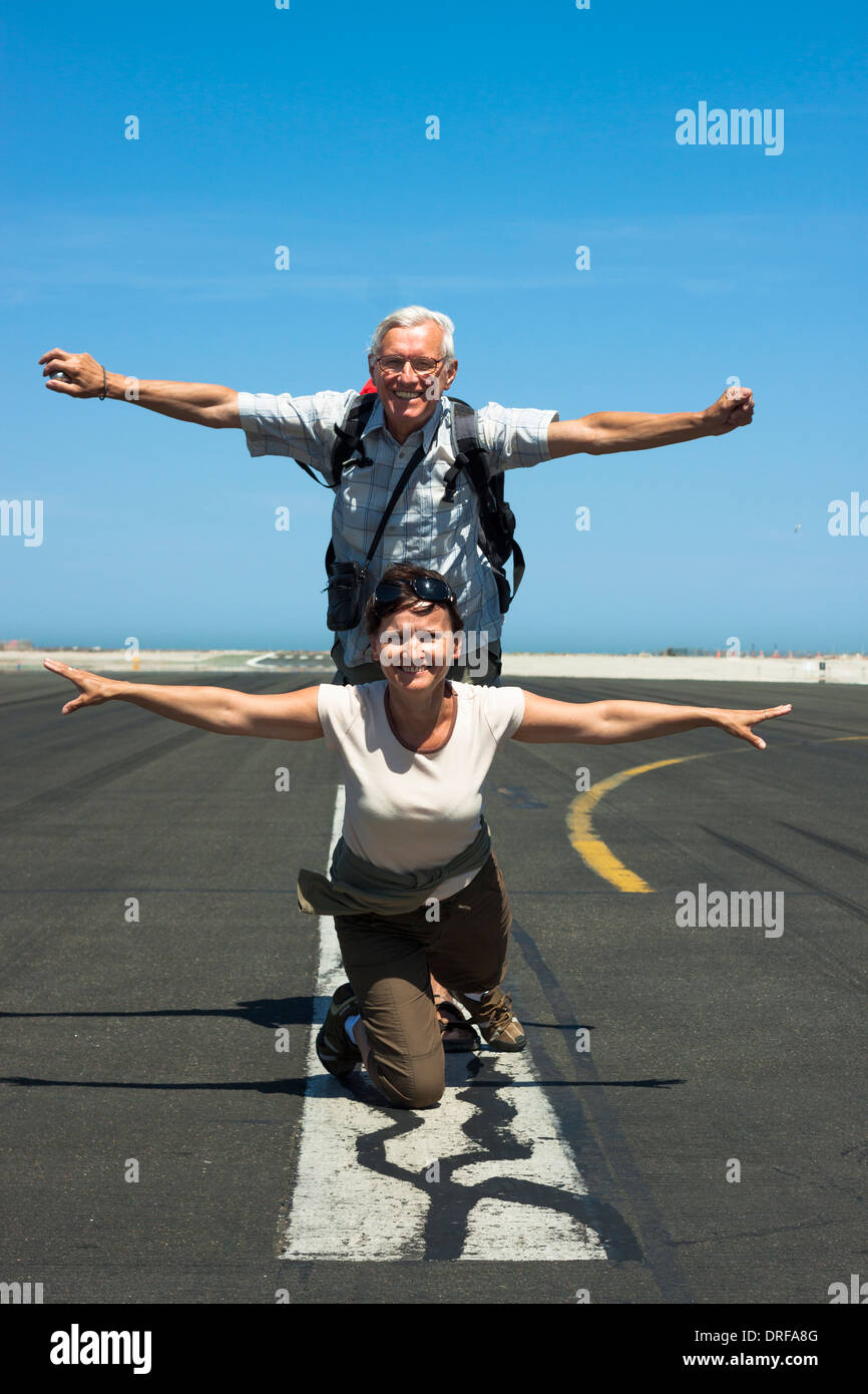 Felice senior l uomo e la donna di mezza età imitando aereo presso la pista di aeroporto Foto Stock