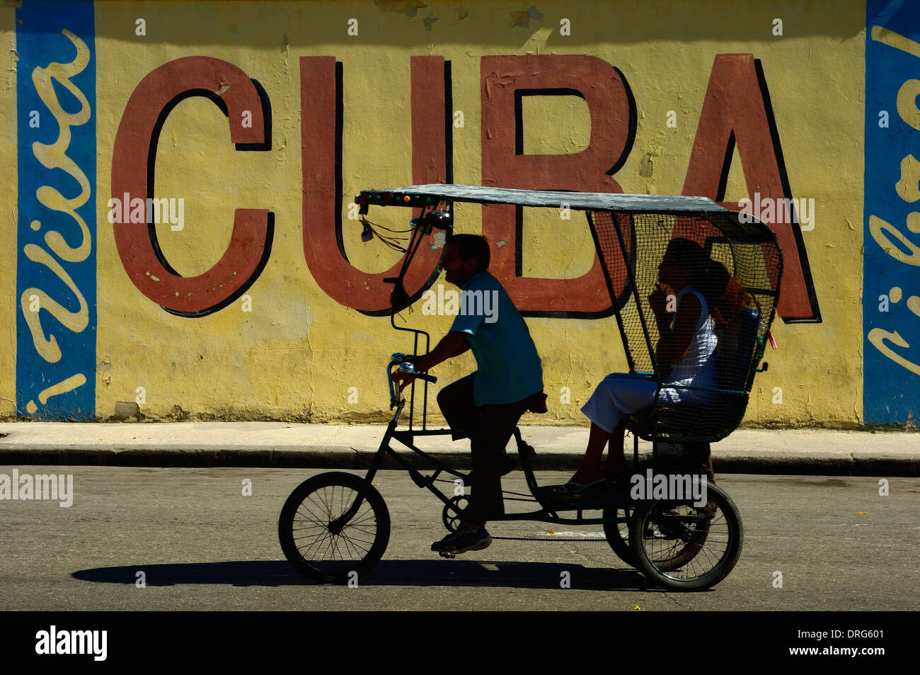 Un rickshaw taxi passando un 'Viva Cuba street segno. L'Avana. Cuba Foto Stock