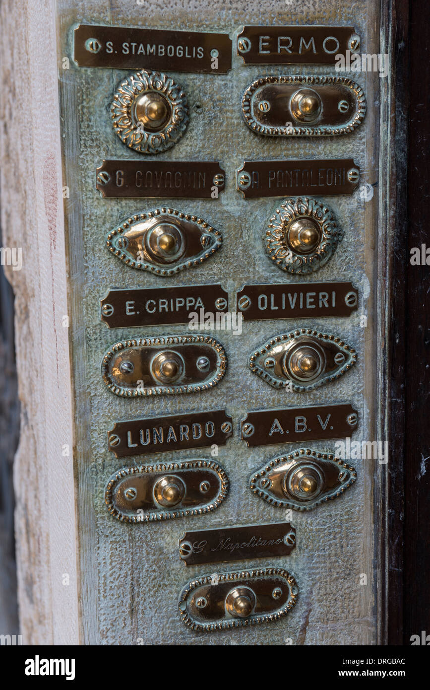 Campanello in ottone i pulsanti e il nome di famiglia piastre su un pannello di ingresso a un palazzo di appartamenti, Venezia, Italia Foto Stock