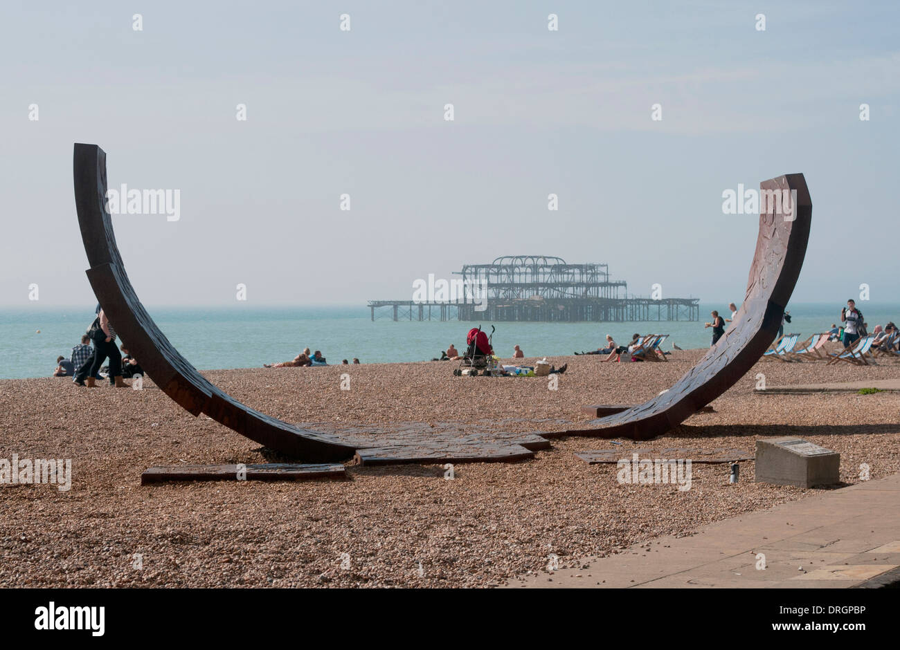 Scultura Moderna sulla spiaggia di Brighton con il vecchio bruciate Brighton Pier a distanza Foto Stock
