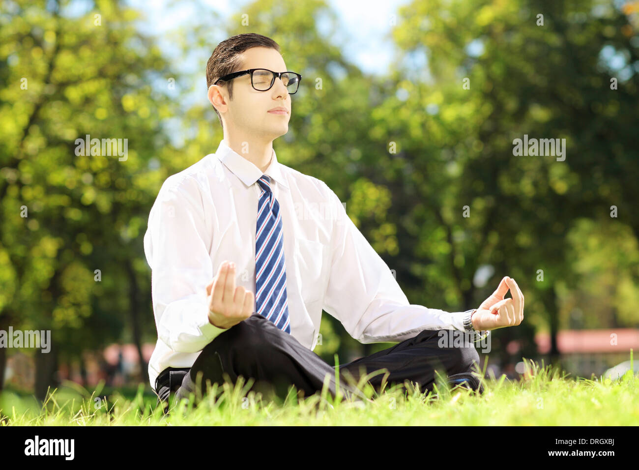 Giovani imprenditori con occhiali meditando seduto su un prato verde in un parco Foto Stock