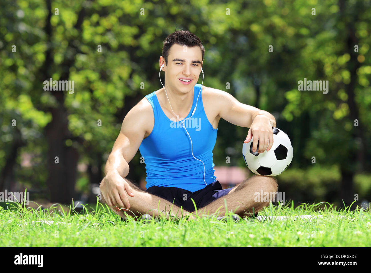 Sorridente giovane atleta maschio seduti su un prato verde con sfera in un parco Foto Stock