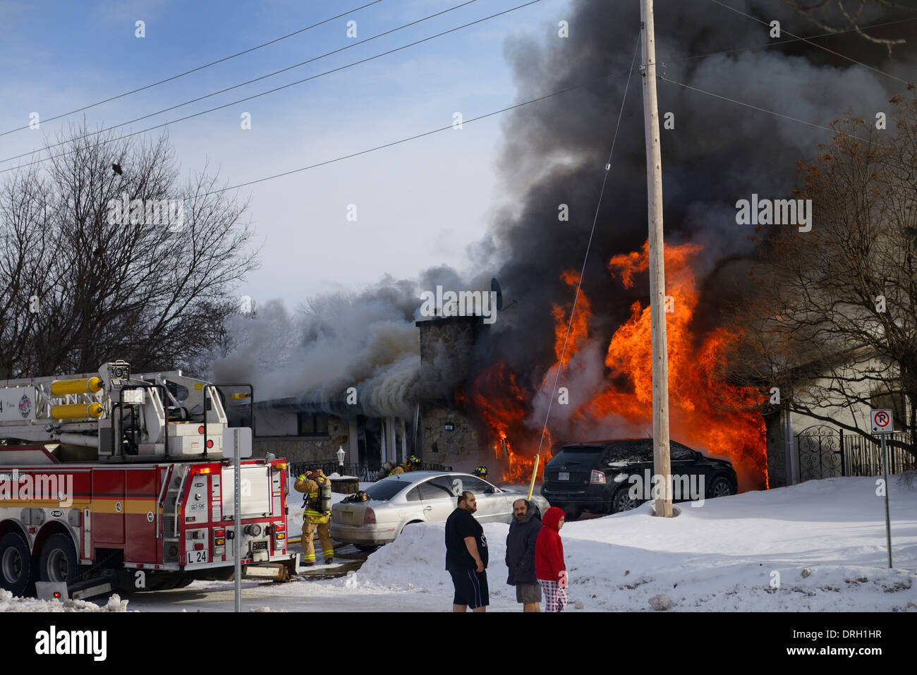 I residenti al di fuori nella notte vestiti in inverno con neve mentre la casa va in fiamme con i vigili del fuoco la spruzzatura di acqua sul fuoco in Ottawa Foto Stock