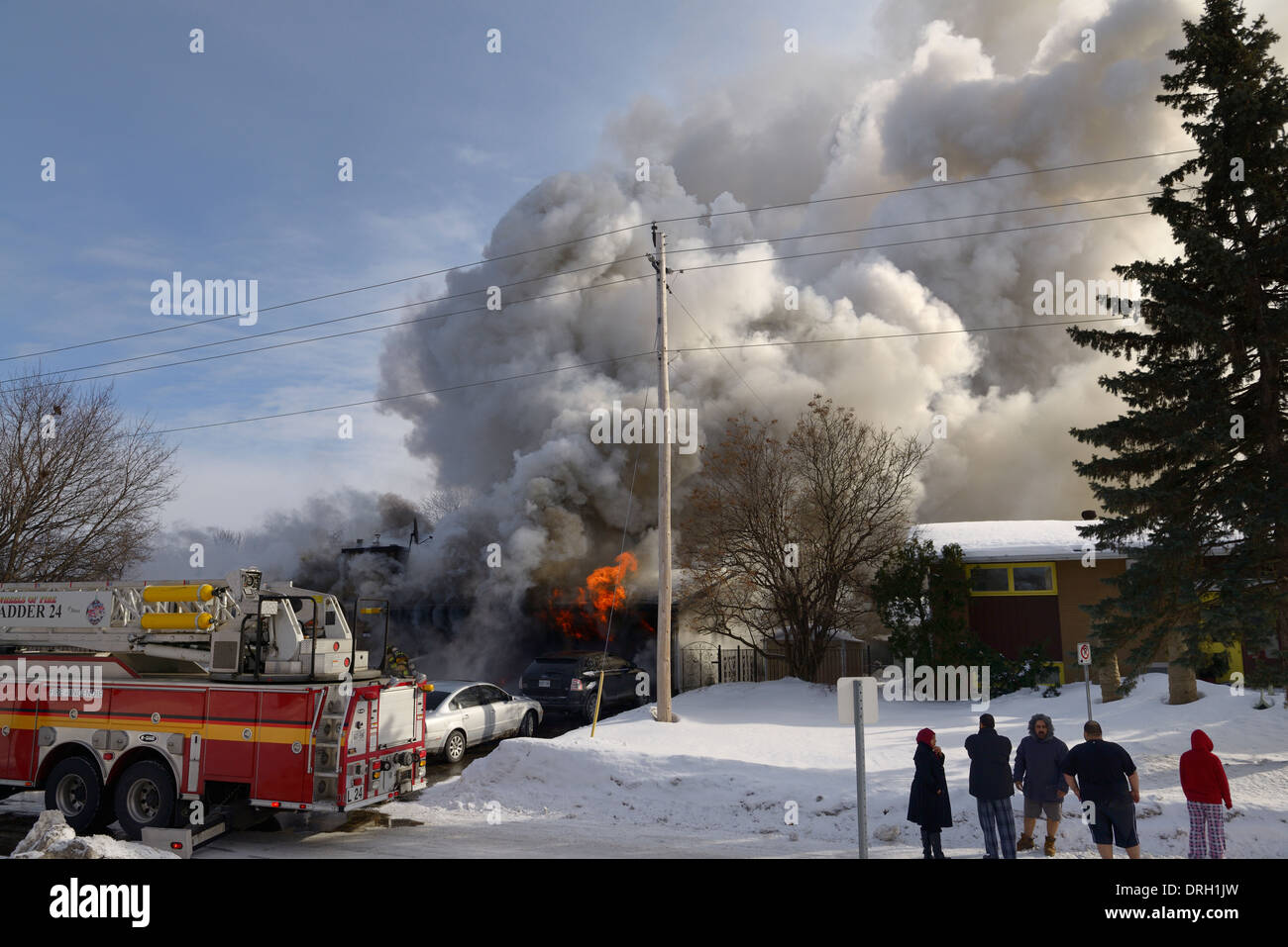 Famiglia al di fuori nella notte vestiti mentre la casa va in fiamme con i vigili del fuoco la spruzzatura di acqua sul fuoco e fumo versando da casa ad Ottawa in Canada Foto Stock