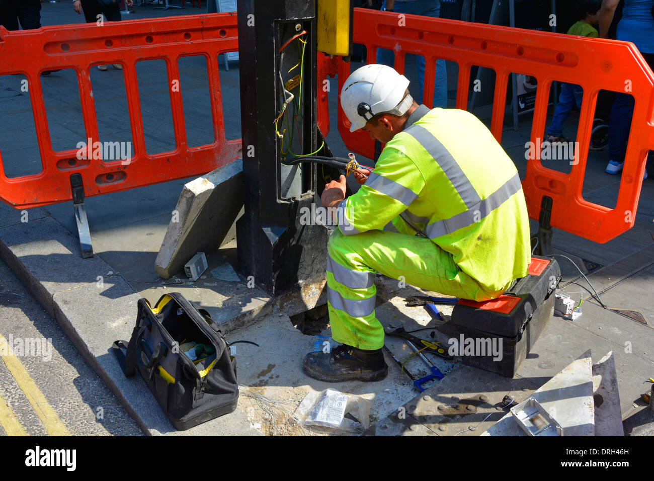 Primo piano di un ingegnere elettricista che lavora su cablaggi e cavi elettrici alla base della colonna di illuminazione stradale scena stradale quotidiana Londra Inghilterra Regno Unito Foto Stock