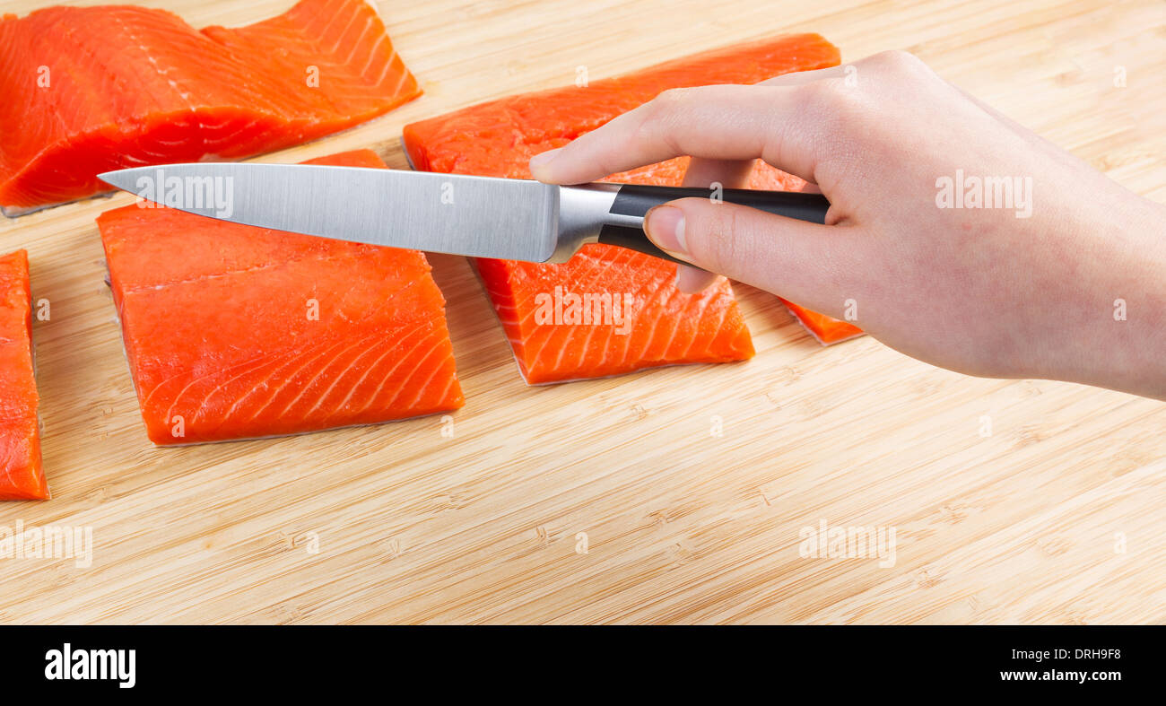 Foto orizzontale di femmine della mano che tiene taglienti dei coltelli di taglio con pezzi freschi di Wild rosso Salmone e bamboo naturale board Foto Stock