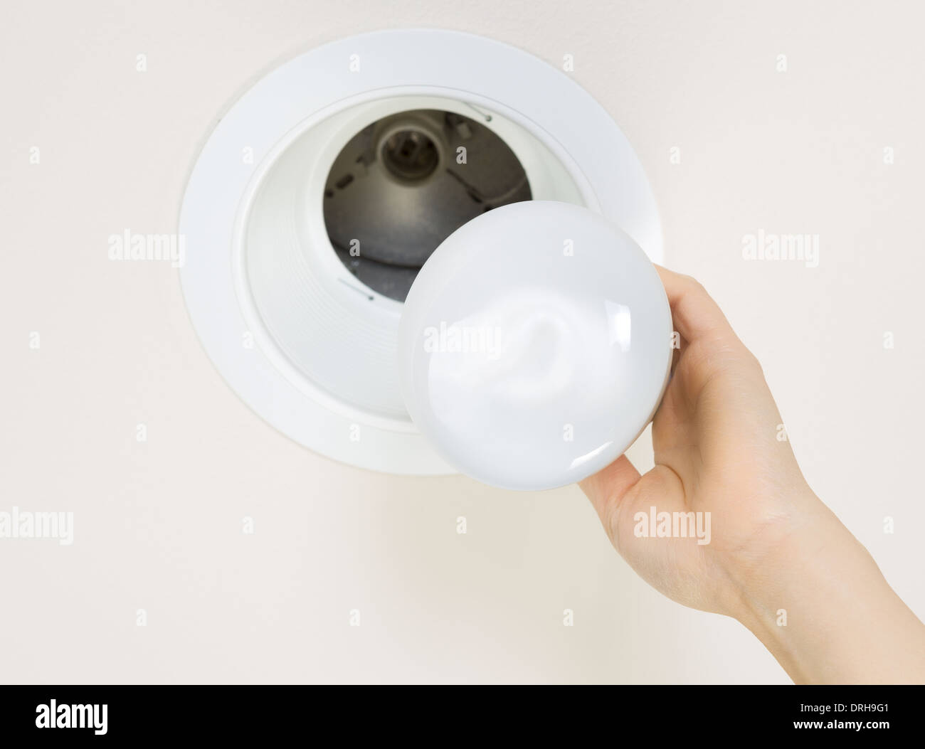 Foto della nuova lampadina del proiettore essendo tenuto dalla mano femminile con incasso a soffitto Montaggio luce in background Foto Stock