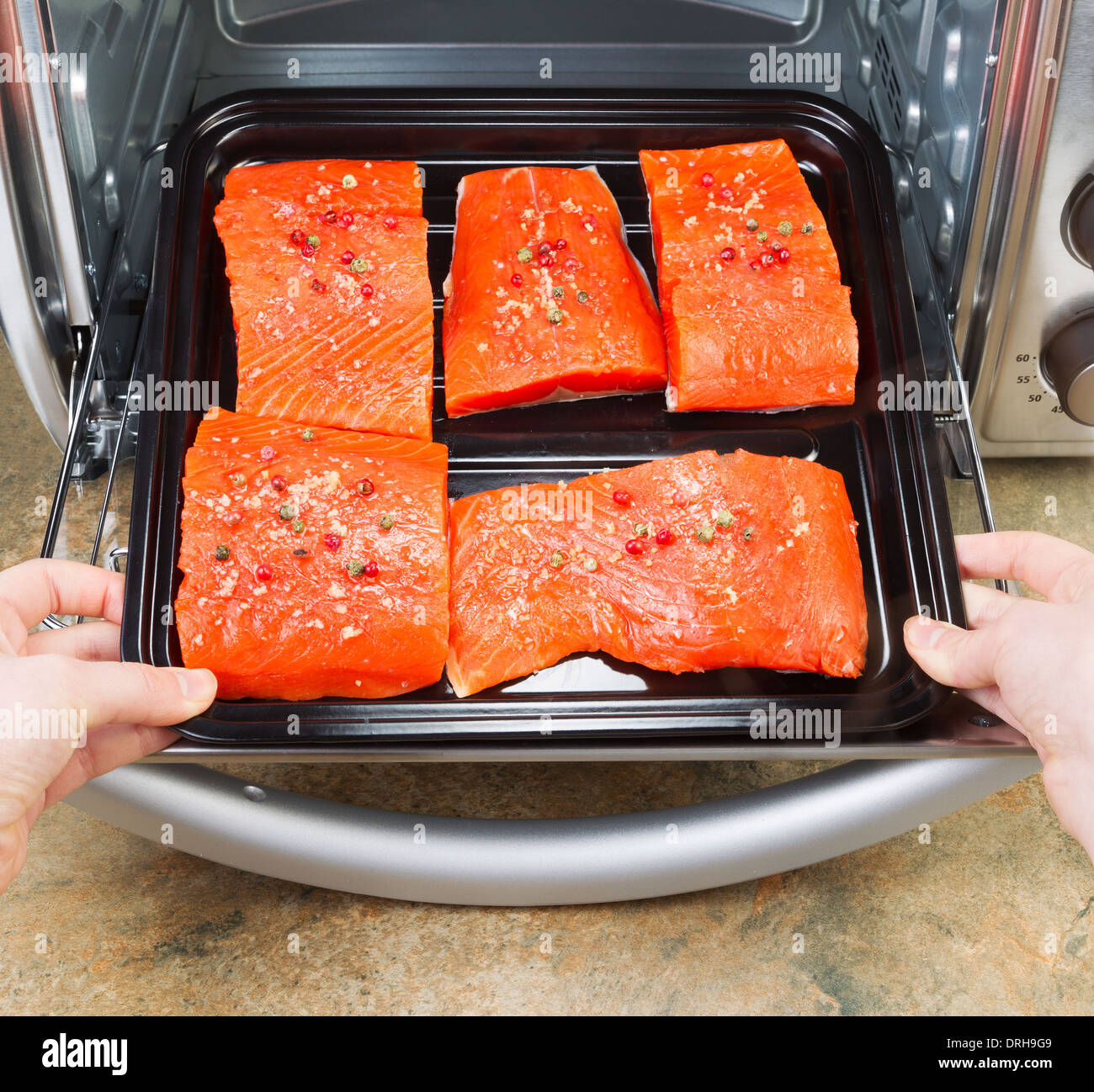 Foto di mani femminili immissione pezzi freschi di Wild rosso Salmone in forno rack con contatore di pietra in alto al di sotto Foto Stock