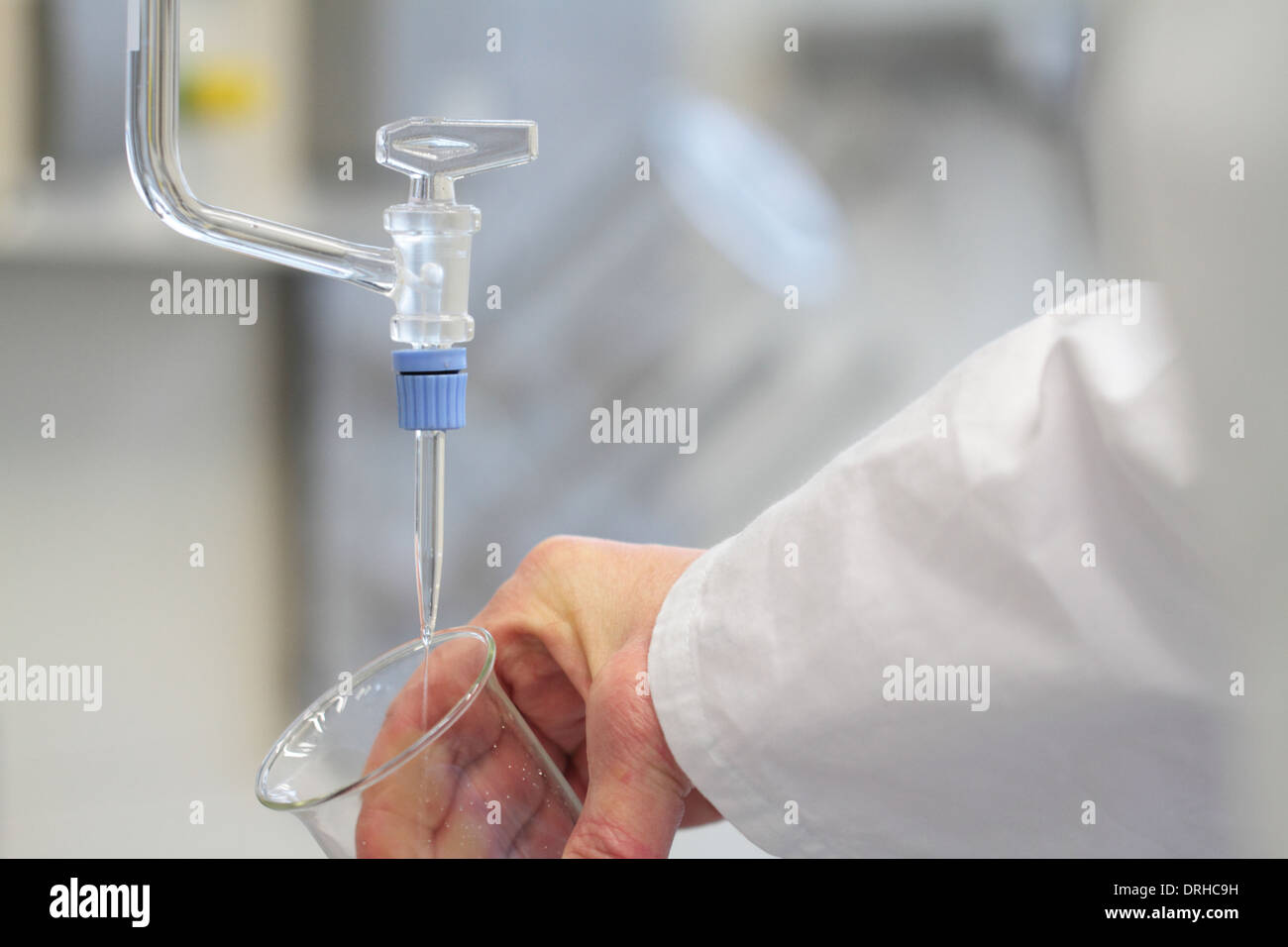 Una mano che tiene un bicchiere di vetro sotto una buretta buretta Foto Stock