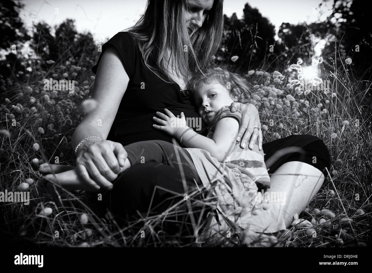 Bambino seduto sulla sua gravidanza della madre giro in un campo durante il tramonto. Foto Stock