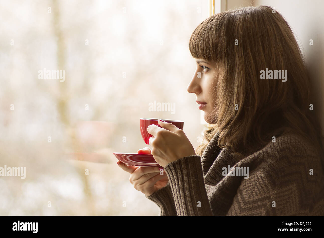 Bella ragazza di bere il caffè o il tè vicino a finestra Foto Stock