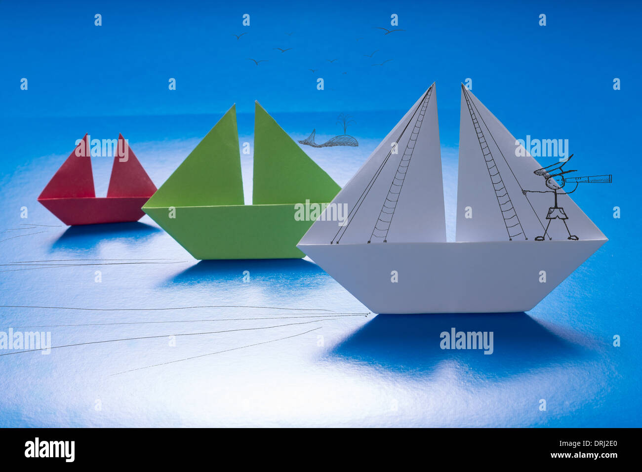 Prelevate il capitano guardando attraverso il cannocchiale su carta in barca a vela con altri su carta blu mare con dettagli disegnati. Origami nave Foto Stock