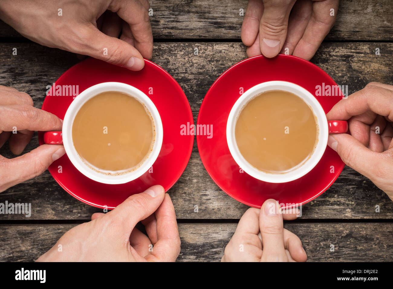 Tenendo le mani rosso due tazze di caffè su uno sfondo di legno vecchio Foto Stock