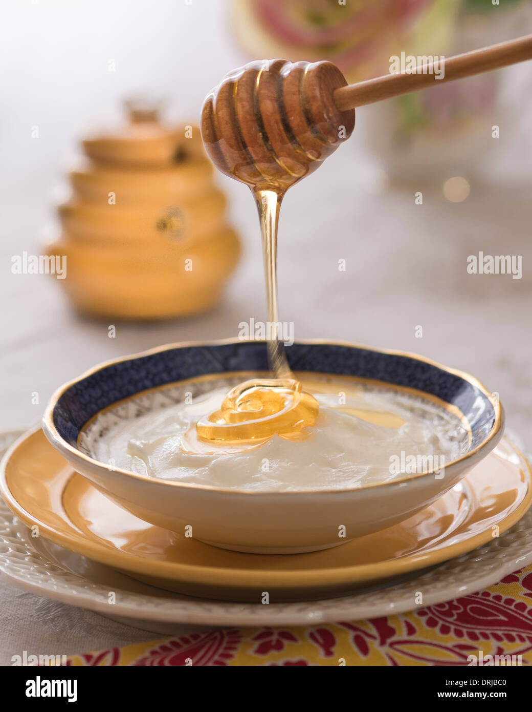 Il miele drizzling oltre lo yogurt con un honey pot in background Foto Stock
