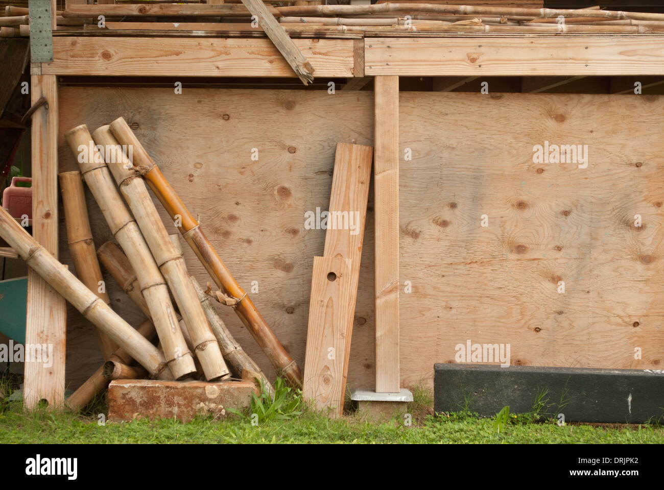 Un mucchio di scarti di legno appoggiata contro un capannone in Hawaii. Alcuni pini e alcuni pezzi di bambù. Foto Stock