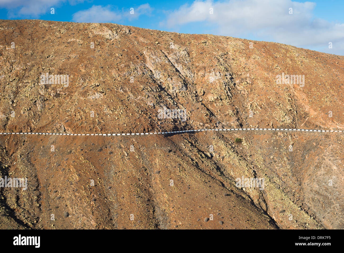 Ripida eroso e stagionato di montagna gabbri, con road delineato dalla protezione blocchi di calcestruzzo, Betancuria, Fuerteventura Foto Stock