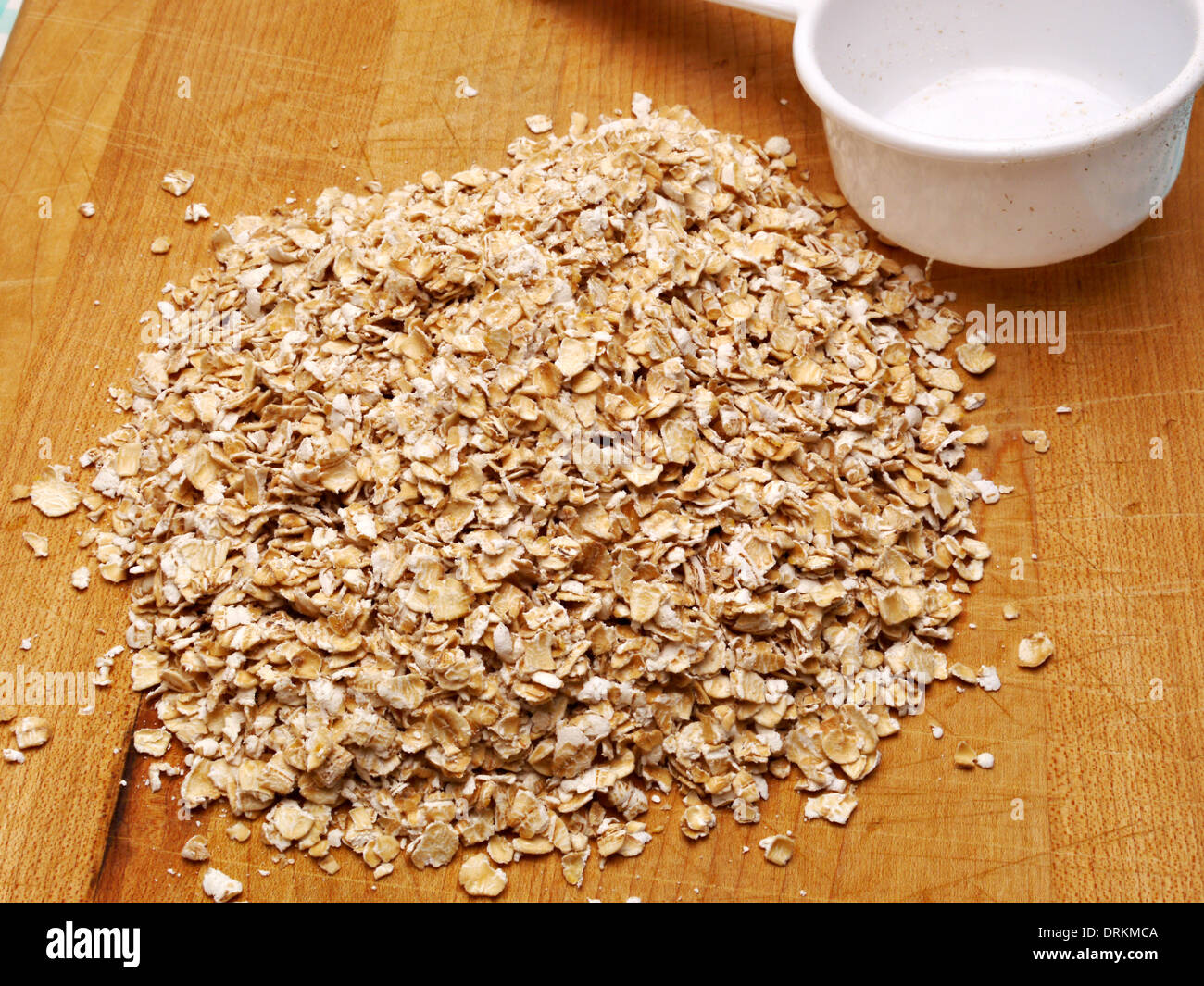 Una pila di fiocchi d'avena cruda si siede su un banco di legno alto. Foto Stock