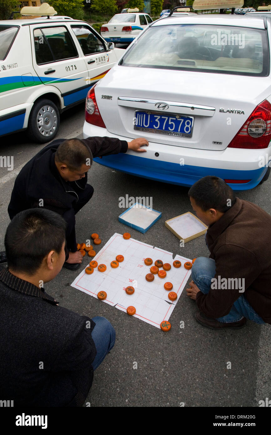 I tassisti cinesi in attesa di passeggeri / tassisti driver si occupano di giocare / giocare una partita di scacchiera cinese Xiangqi in strada con le loro auto taxi. Cina Foto Stock