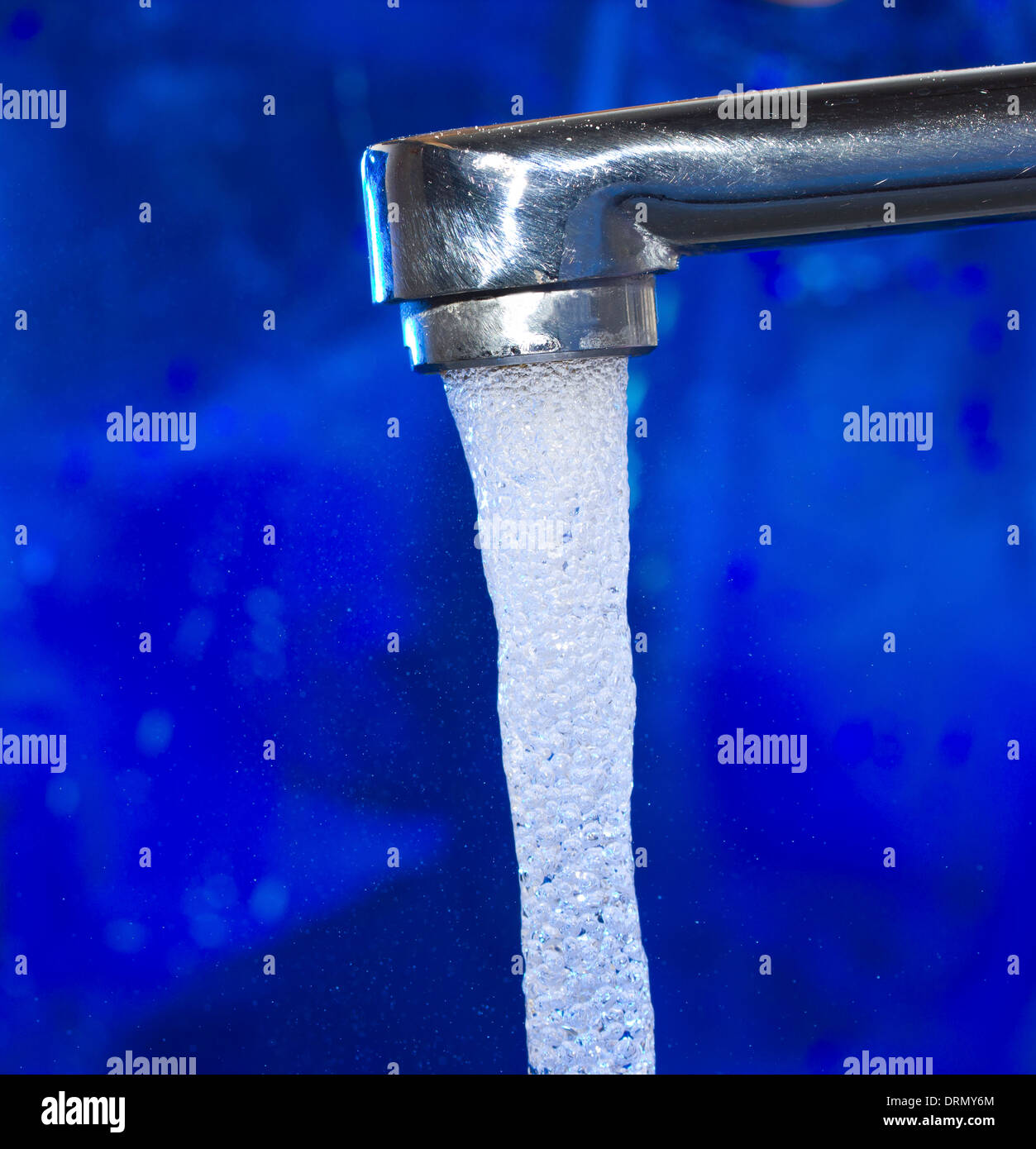 Flusso di acqua da un rubinetto su sfondo blu Foto Stock