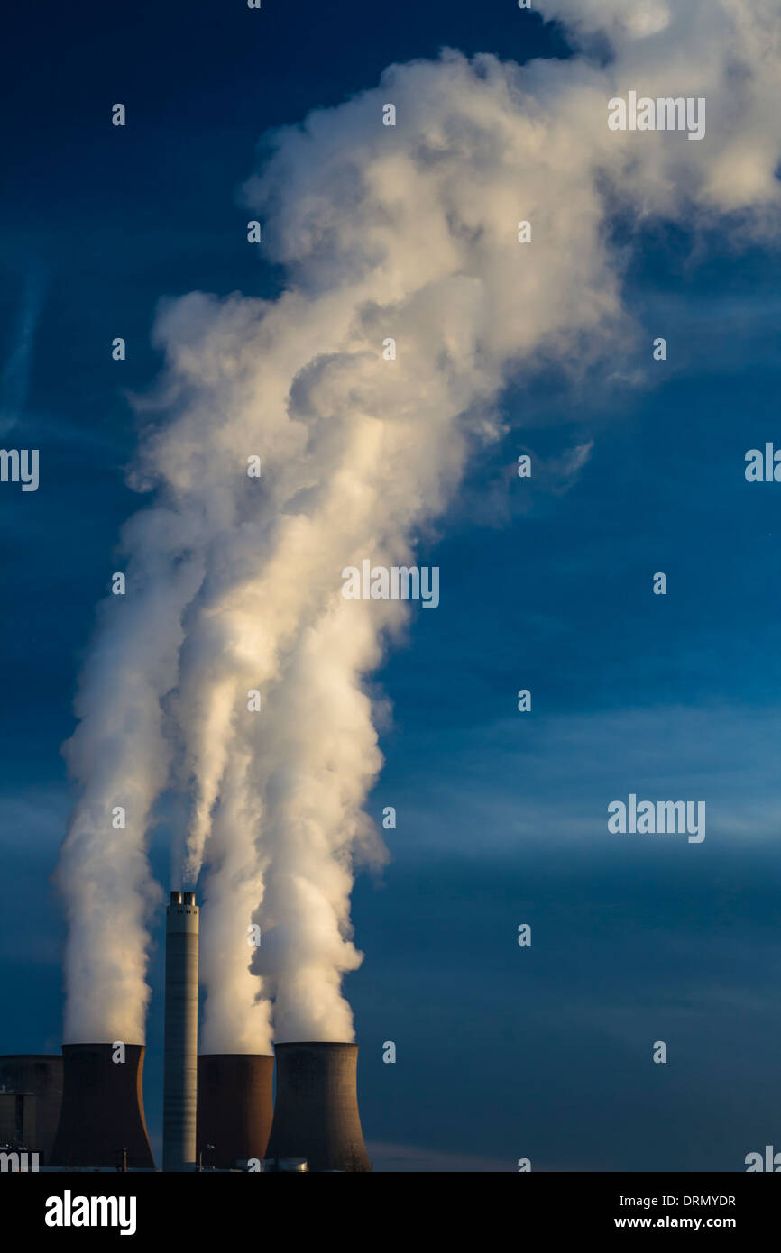Una drammatica vista delle torri di raffreddamento di una stazione di alimentazione a piena potenza, ondeggianti tall pennacchi di fumo in un cielo blu chiaro. Foto Stock