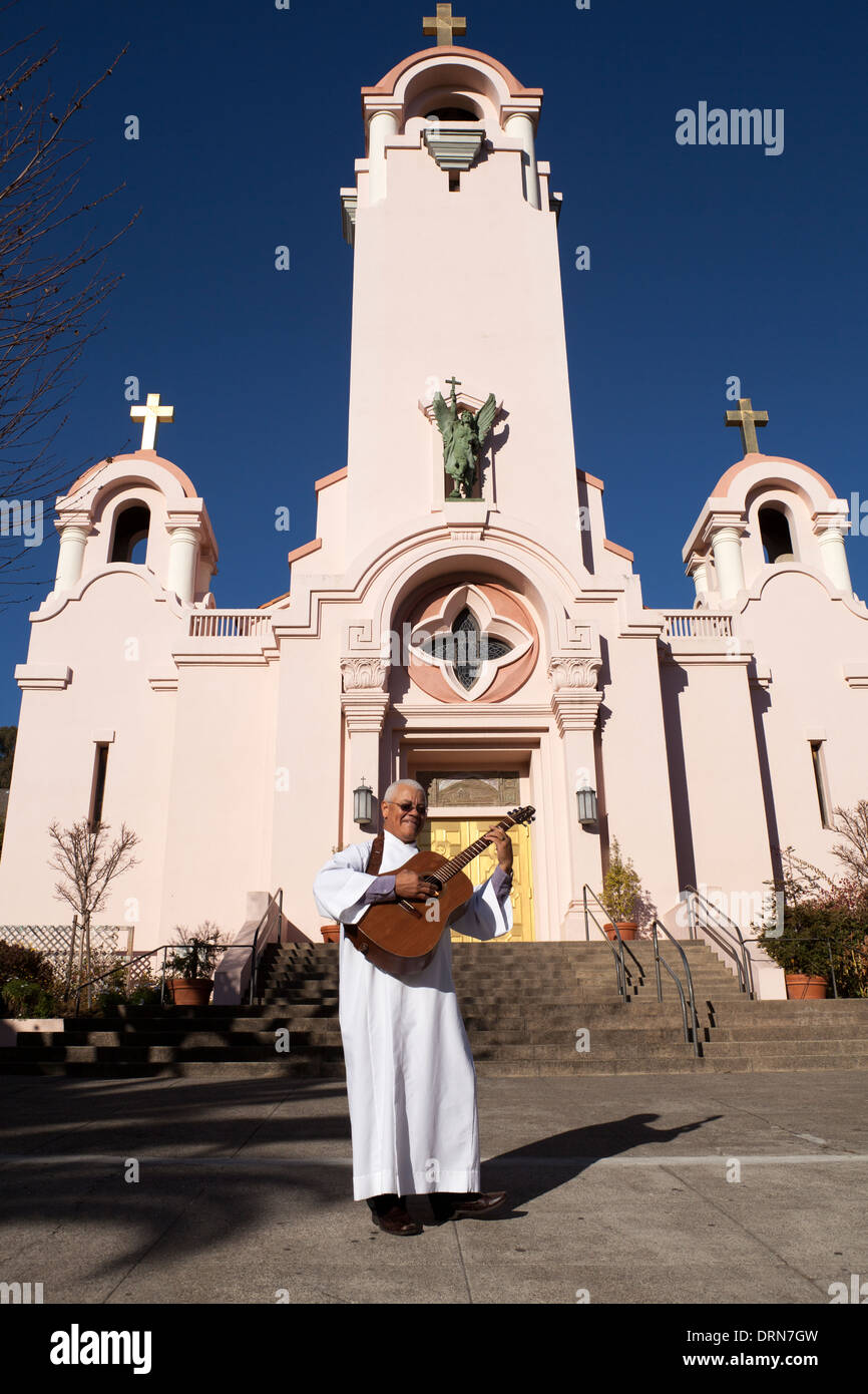 Sacerdote a suonare la chitarra di fronte al San Rafael Arcángel chiesa cattolica, San Rafael, California, USA, America del Nord. Foto Stock