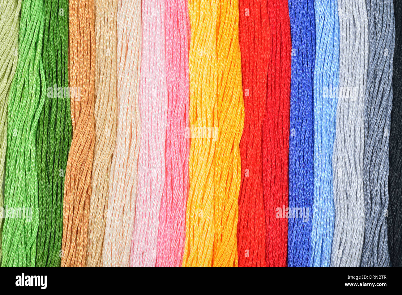 Colorati fili di ricamo in una fila. Sfondo colorato. Foto Stock