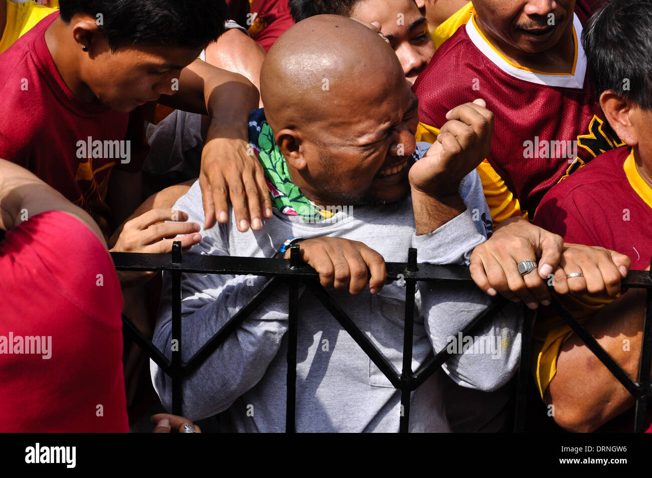 Un uomo è premuta contro una recinzione da spintoni devoti durante la processione del Nazareno nero a Manila. Foto Stock Un uomo è premuta contro una recinzione da spintoni devoti durante la processione del Nazareno nero a Manila. Foto Stock