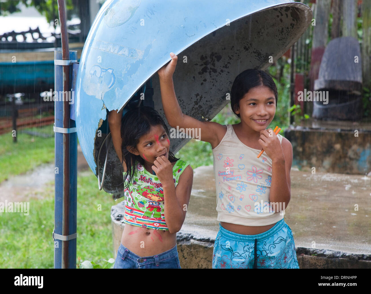 Due ragazze timide riparo dalla luce di una doccia a pioggia in una cabina telefonica la copertura meteo in Pacoval village, l'Amazzonia, Brasile Foto Stock