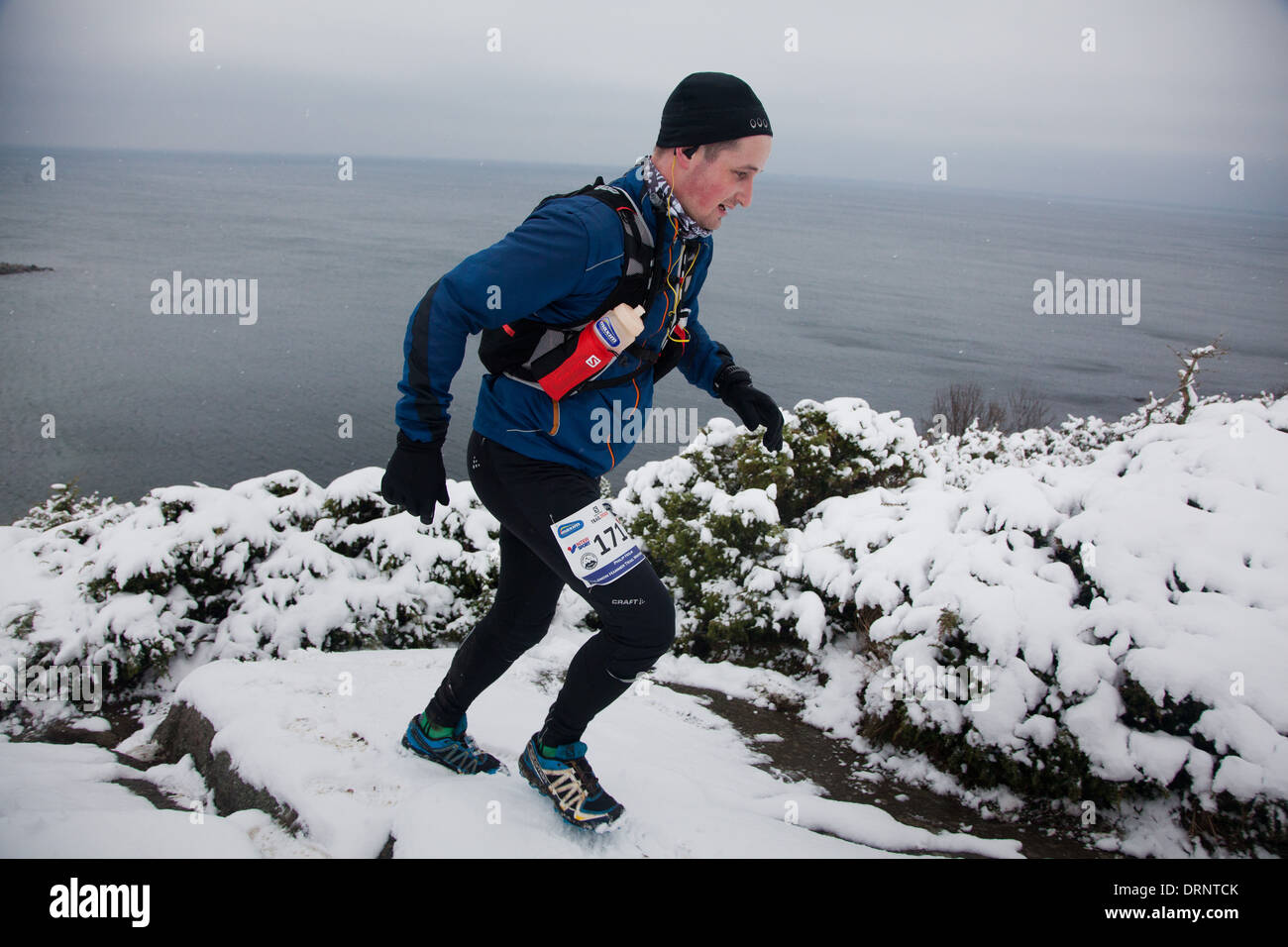 Un runner fa il suo modo fino a snowy percorso roccioso dalla linea di costa del nord Bornholm. Foto Stock