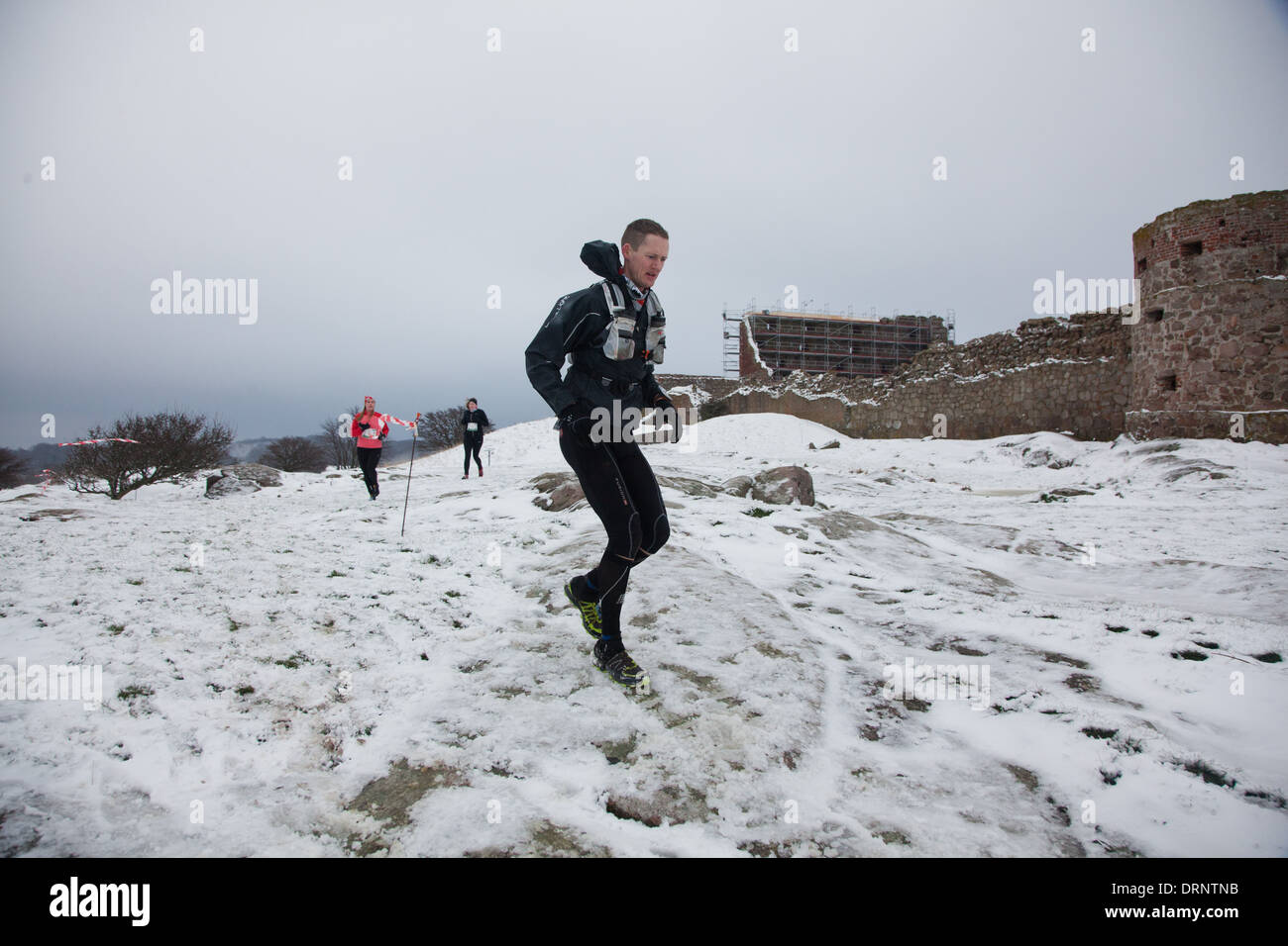 Runner facciano il loro modo attraverso terreni innevati e rocce ghiacciate passato Hammershus. Foto Stock