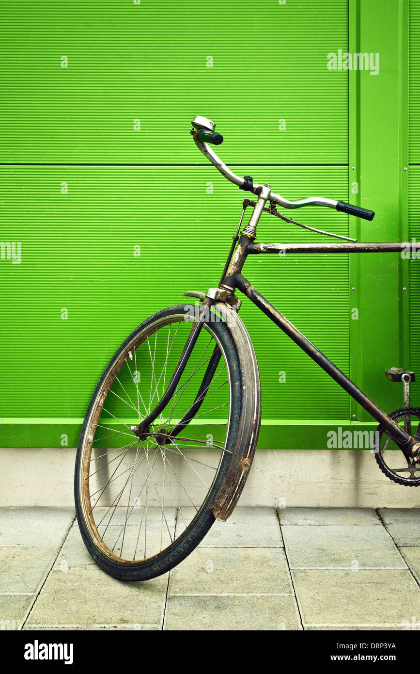 Vecchia bicicletta appoggiata sulla parete verde il vecchio incontra il nuovo concetto. Foto Stock