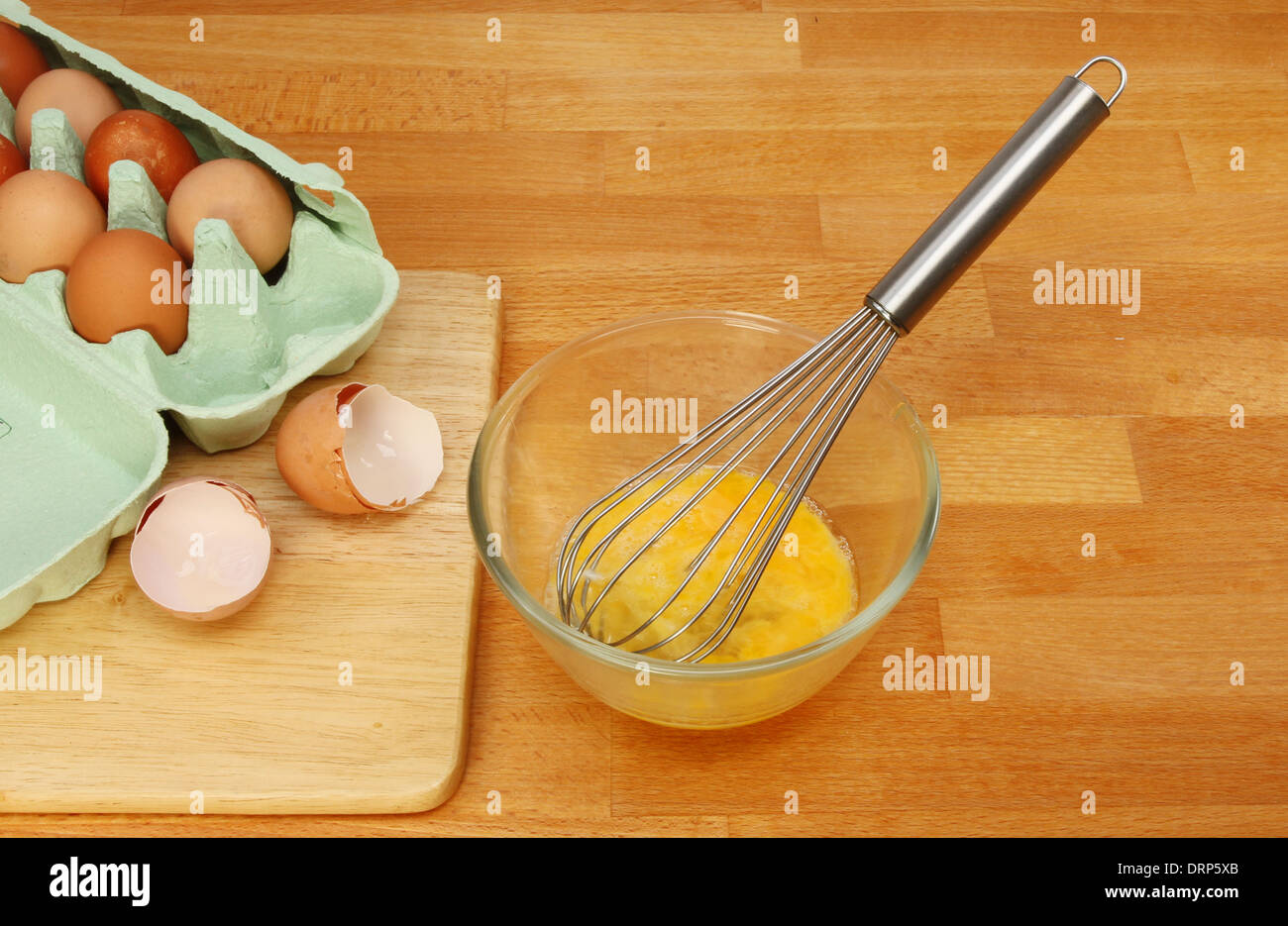 Battere le uova, le uova in un recipiente di vetro con una frusta su una cucina in legno piano di lavoro Foto Stock