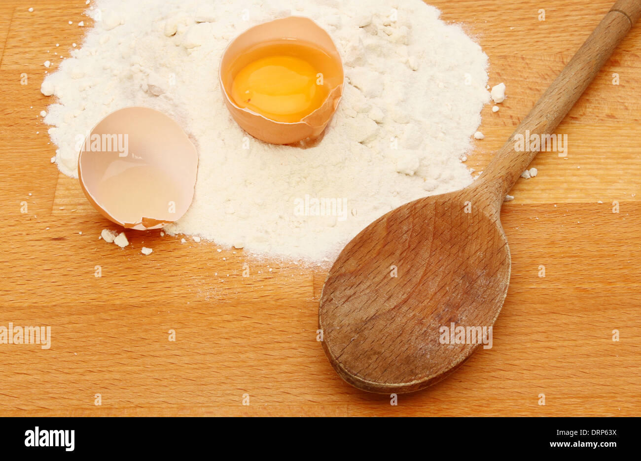 Farina, uova e un cucchiaio di legno su una cucina in legno piano di lavoro Foto Stock