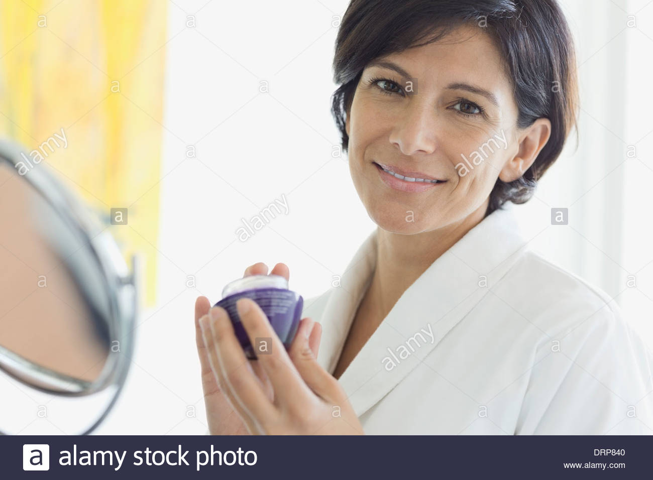 Donna che mantiene crema contorno occhi nella stanza da bagno Foto Stock