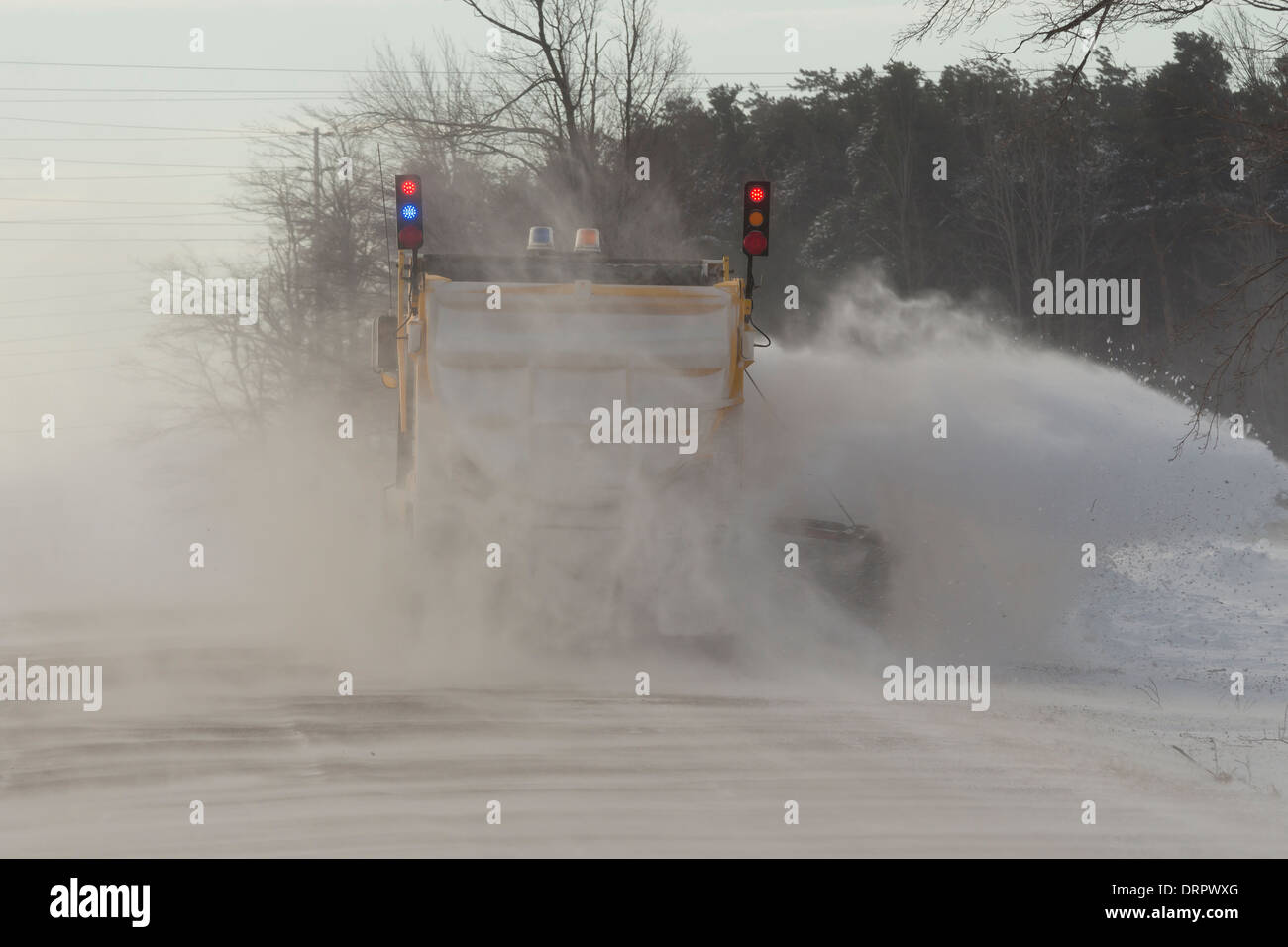 Un giallo Snow Plough cancella una strada in condizioni di blizzard come soffiata dal vento coperto di neve la strada creando grandi derive Foto Stock