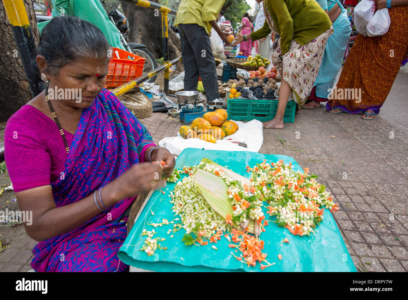 Una donna che fa floral decorazioni capelli ad una strada del mercato di Mysore, India. Foto Stock