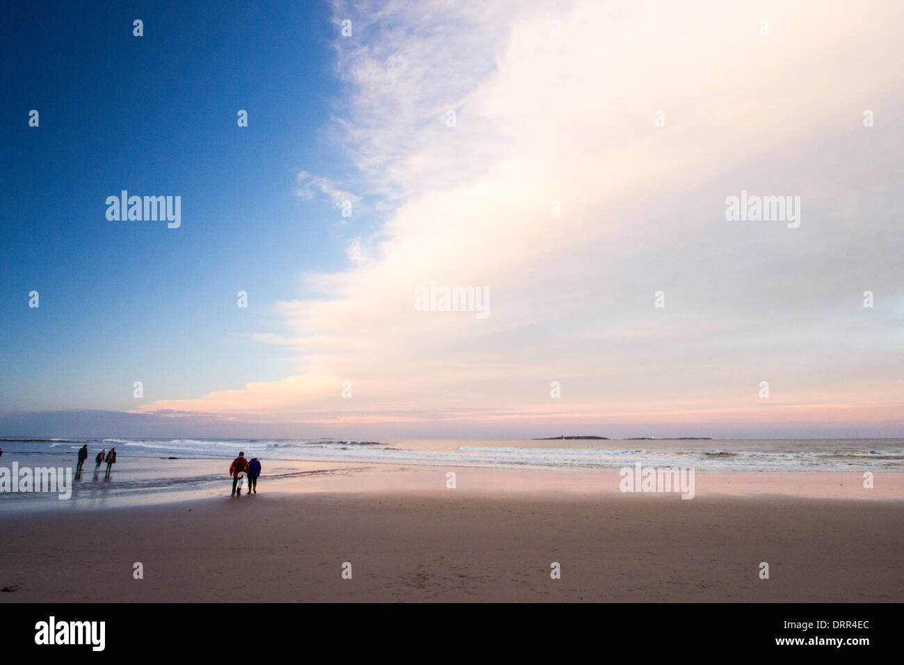 Walkers sulla spiaggia al tramonto vicino Seahouses, Northumberland, Regno Unito. Foto Stock