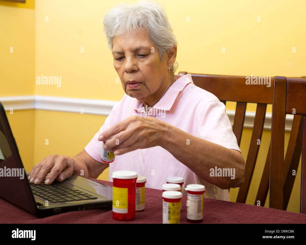 75 anni femmina ispanica senior citizen utilizzare il computer portatile per ordinare i farmaci di prescrizione ad un on-line farmacia Foto Stock