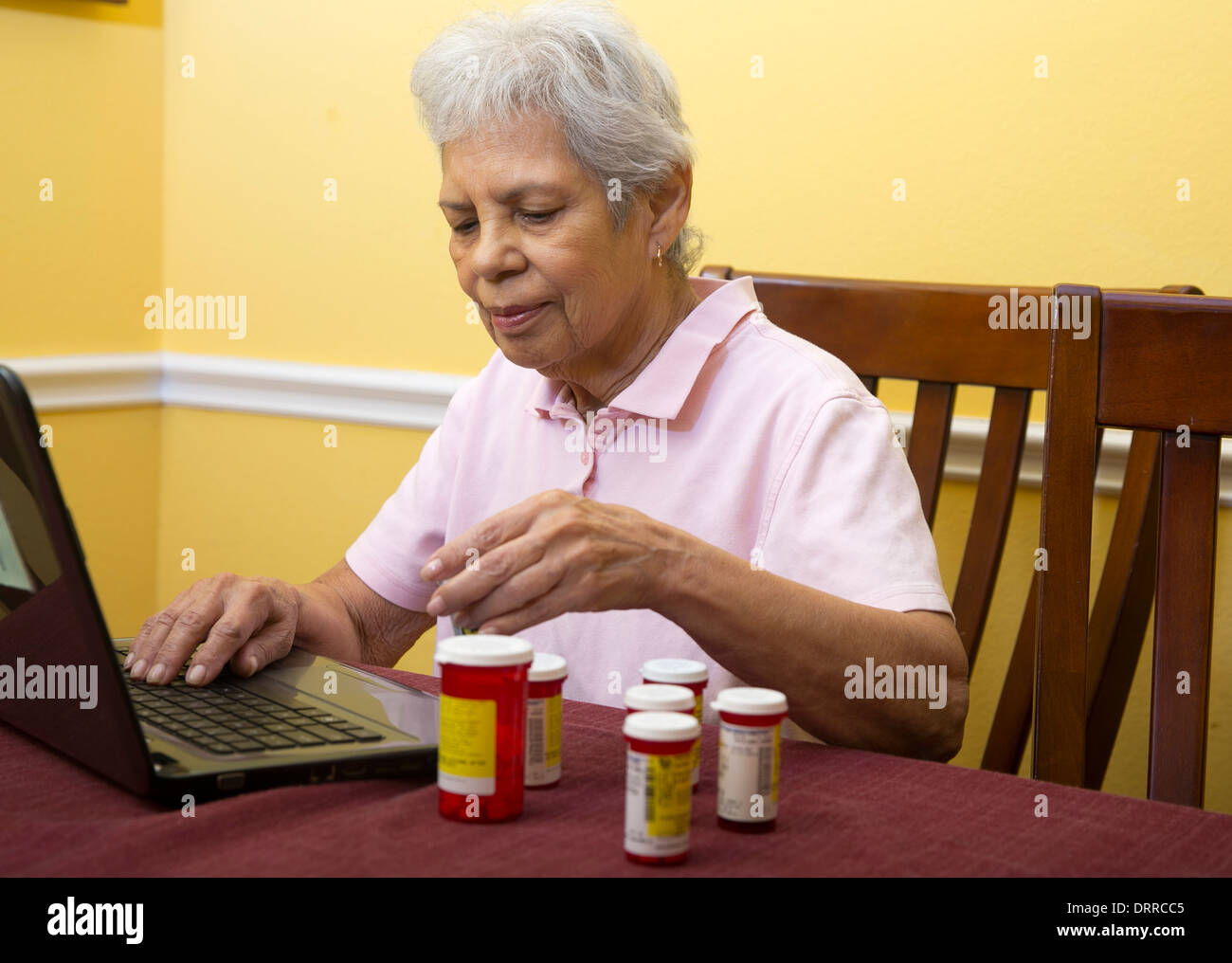 75 anni femmina ispanica senior citizen utilizzare il computer portatile per ordinare i farmaci di prescrizione ad un on-line farmacia Foto Stock