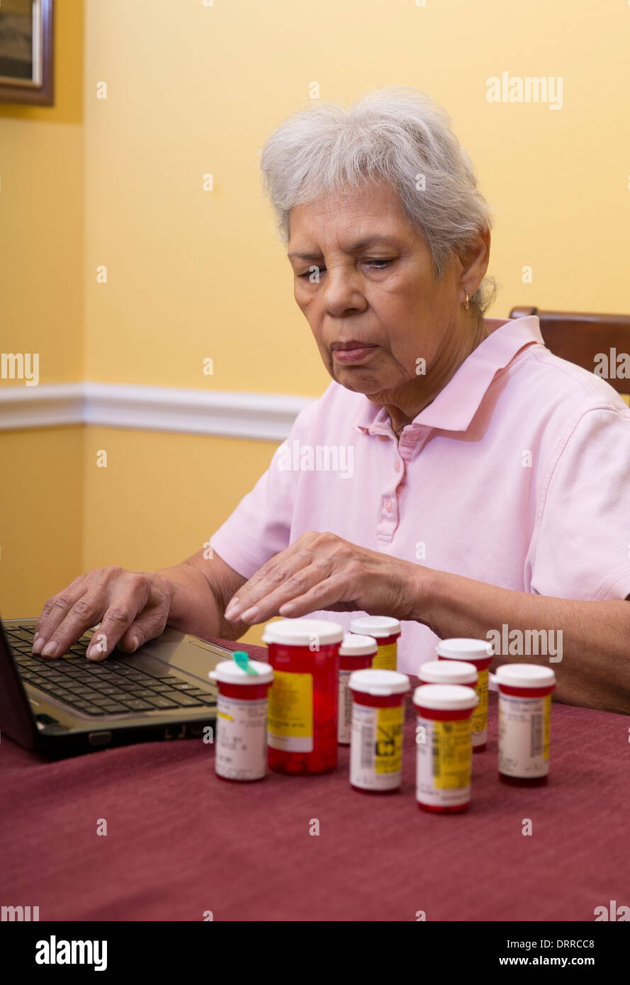 75 anni femmina ispanica senior citizen utilizzare il computer portatile per ordinare i farmaci di prescrizione ad un on-line farmacia Foto Stock