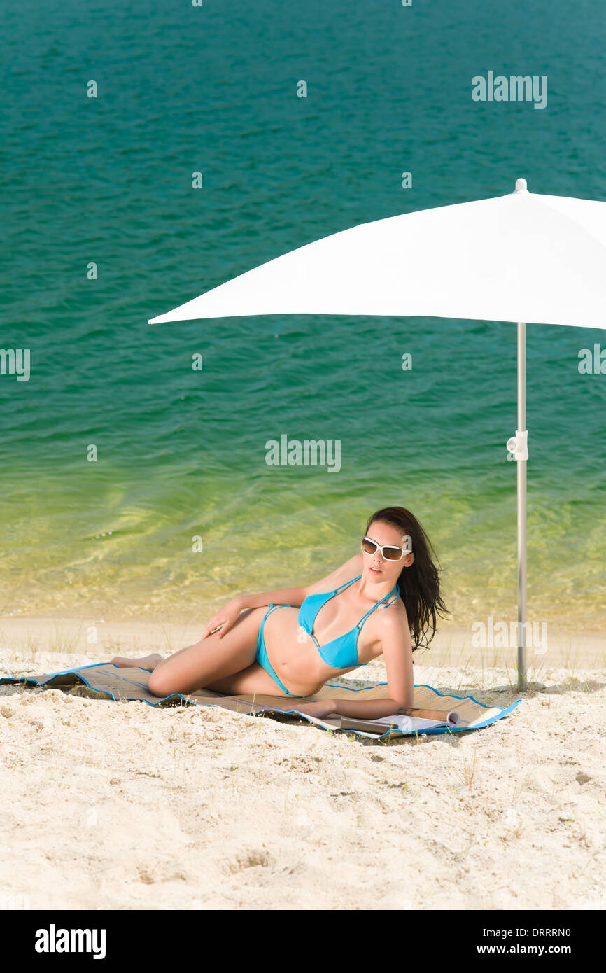 Estate spiaggia donna bikini blu sotto ombrellone Foto Stock