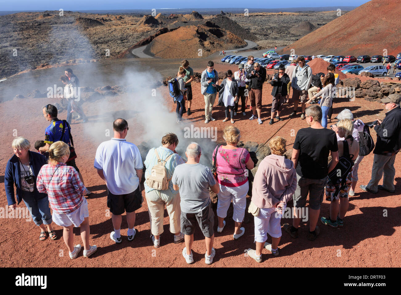 I turisti guarda una dimostrazione di calore dall'apertura vulcanica in Montanas del fuego Parco Nazionale Timanfaya, Lanzarote, Isole Canarie Foto Stock